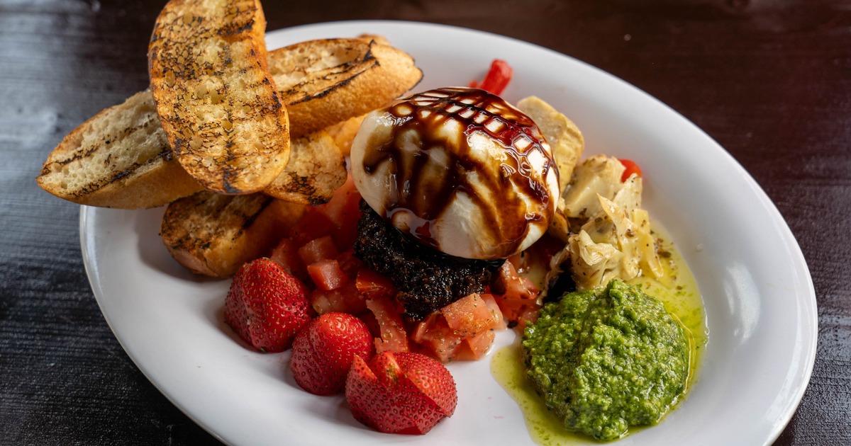 Burrata appetizer drizzled with balsamic glaze, served with various condiments and toast