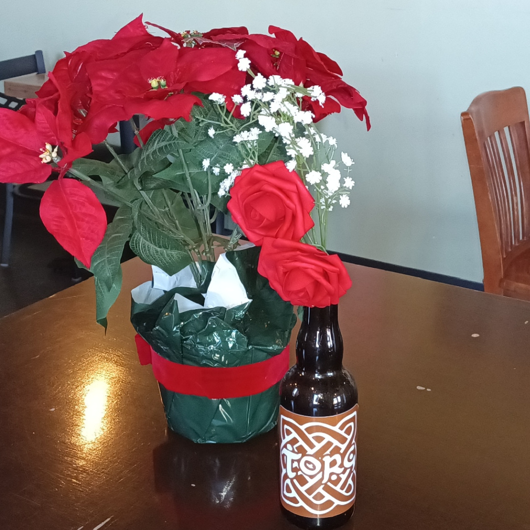 Bouquets of roses and sweet alyssums in a green plastic-wrapped pot and a beer bottle with a 