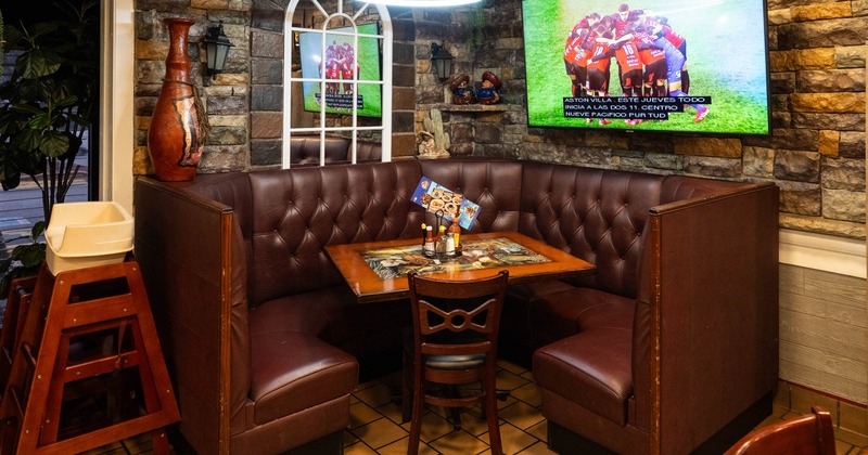 Restaurant booth with tufted brown leather seating, a wooden table, and a TV showing a soccer game