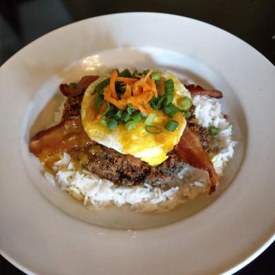 Rice topped with a veggie patty, crispy bacon, an egg over easy, and scallions.