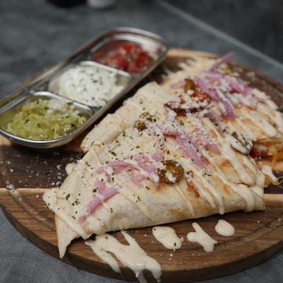 Quesadilla served on a wooden board accompanied by various dips.
