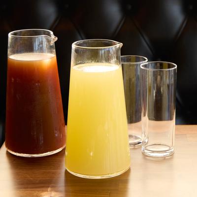 Two glass pitchers filled with juices sit on a table, accompanied with two empty glasses.