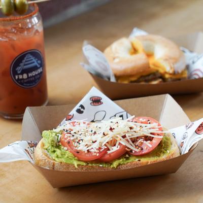 Avocado toast, breakfast sandwich, and cocktail on a wooden table.