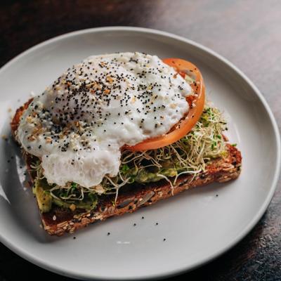 Avocado toast topped with sprouts, tomato, and seasoned poached egg.