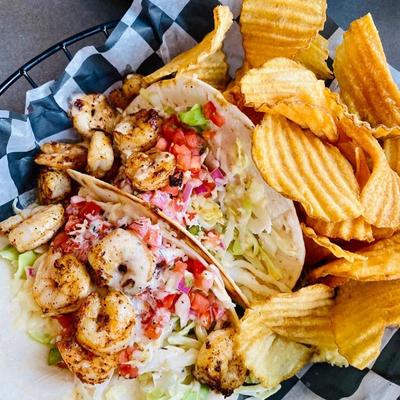 Shrimp tacos with various toppings, served with chips.