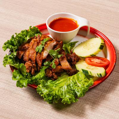 Fried chicken slices on lettuce with cucumber, tomato, and red dipping sauce.