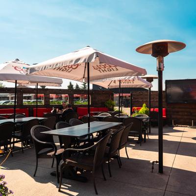 Sunlit patio featuring tables, chairs, umbrellas, and heaters.
