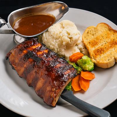 Baby back ribs served alongside mashed potatoes, steamed veggies, brown gravy, and toast.