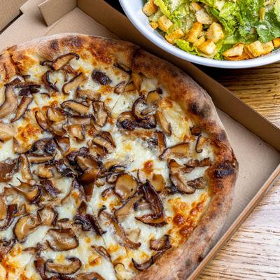 Mushroom pizza in a box beside a bowl of Caesar salad.