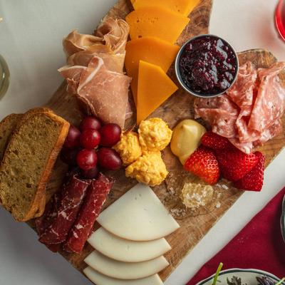 Charcuterie board with assorted cured meats, cheeses, brad, fruits, jam.