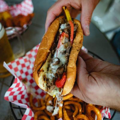 Grilled Steak Philly being held over a basket of onion rings.