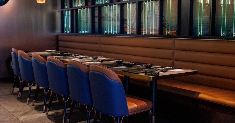 A modern restaurant dining area with blue chairs, a reserved table, and pendant lights