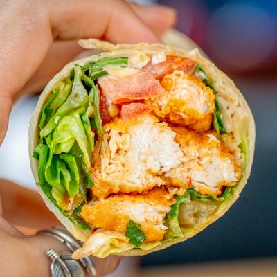 A hand holds a fried chicken wrap.