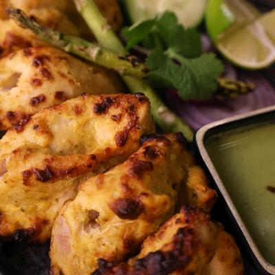Malai Chicken Tikka served with a green mint-coriander chutney and fresh garnish.