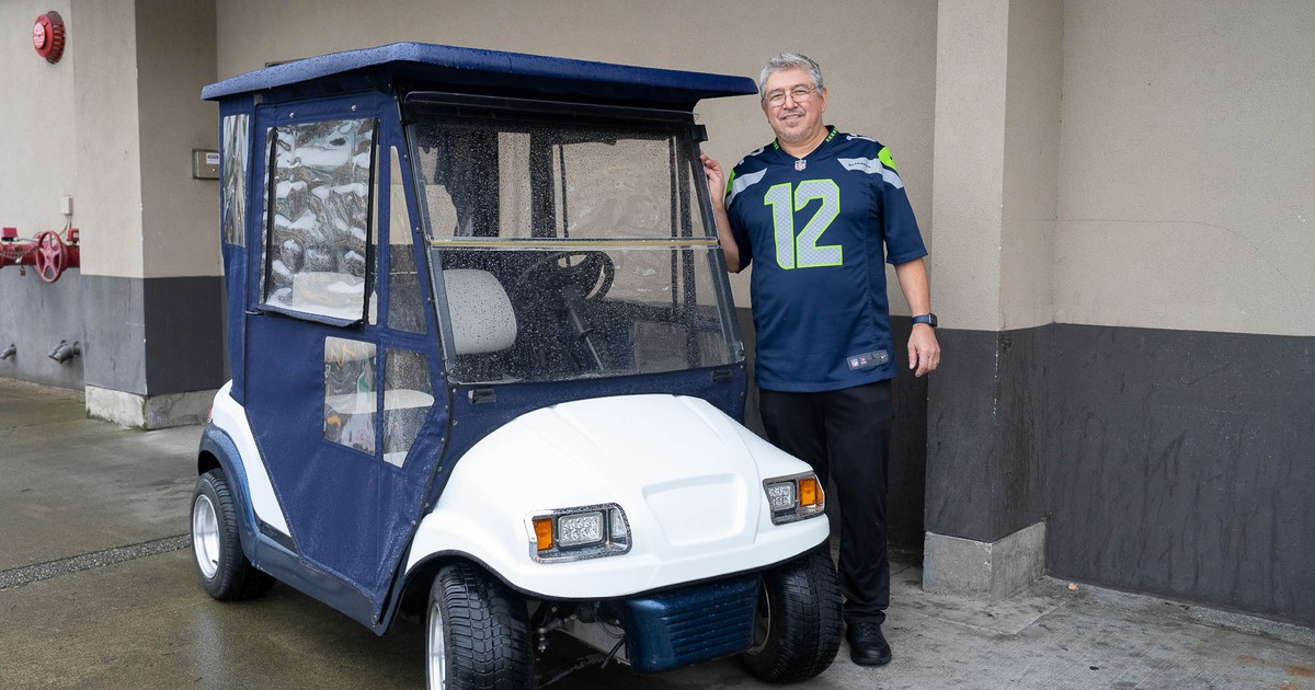 Person wearing s Seattle Seahawks jersey is standing beside a golf cart