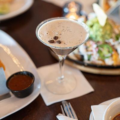 Espresso Martini surrounded by food plates, close up shot.