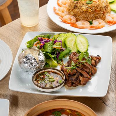 Plate of Thai Grilled Pork with sides, alongside Garlic Shrimp Fried Rice and a drink.