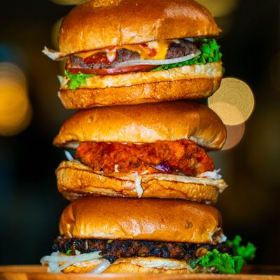 A stack of three fully loaded burgers on a wooden serving tray.