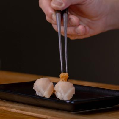 Chef adding crunchy topping on scallop sushi.