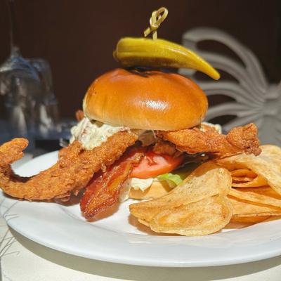 Fried flounder sandwich with bacon, lettuce, tomato, and chips on the side