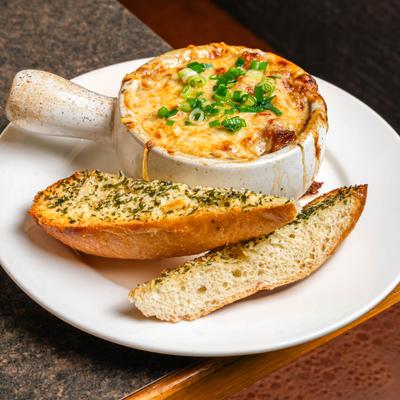 A bowl of baked french onion soup with garlic bread on the side.