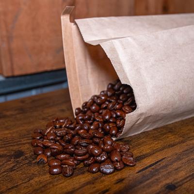 Coffee beans spilling from a beige paper package onto a wooden surface.