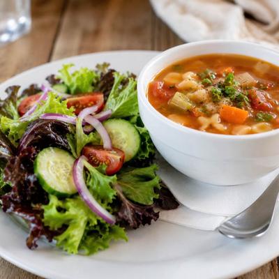 Minestrone soup served in a white bowl, paired with a fresh side salad.