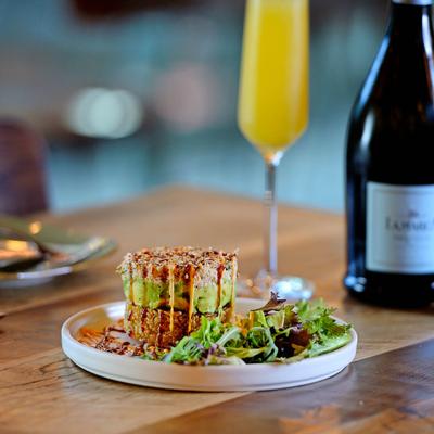 A tuna tower served with a mimosa with a bottle of champagne in the background.