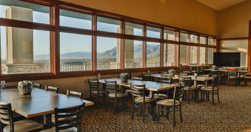 Dining room, large windows, wooden tables and black chairs, small flower vases on the tables