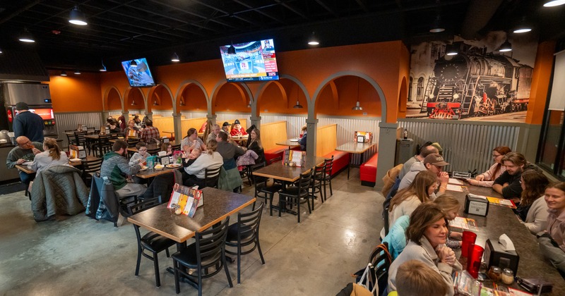 Dining room full of guests, TV screens above booths
