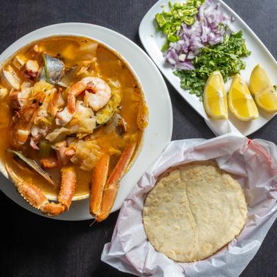 Bowl of Seafood Soup served with lime wedges, cilantro, onion, jalapenos and tortillas.