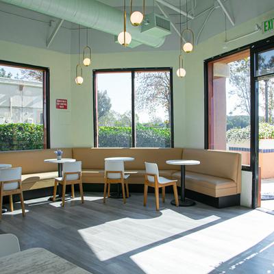 Bright interior with a leather banquette, tables, large windows, and pendant lights.