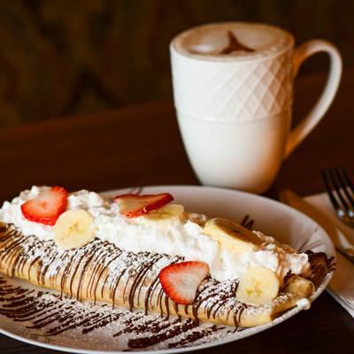 Strawberry Banana Crepe and a cappuccino on a table.