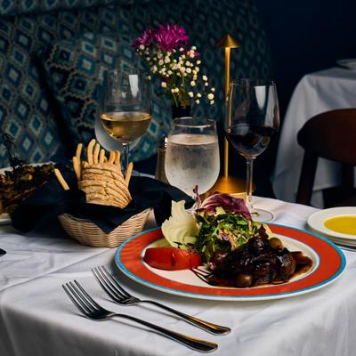 Steak dinner beside bread basket and wine glasses.