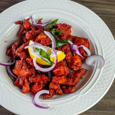 Red fried chicken topped with sliced red onions, herbs, and a lemon wedge.