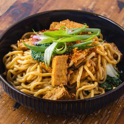 Garlic noodles with tofu, served in a black plate on a wooden table.