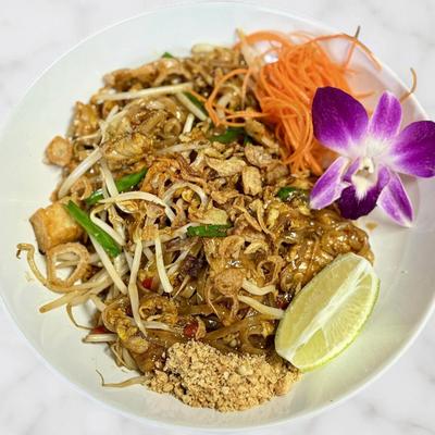 A plate of savory Pad Thai noodles garnished with crushed peanuts and lime.