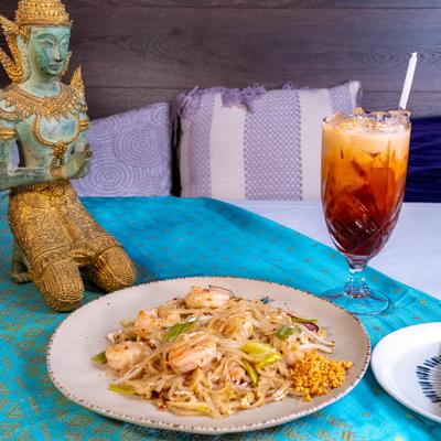 Plate of Pad Thai noodles with shrimp, served alongside a glass of Thai iced tea.