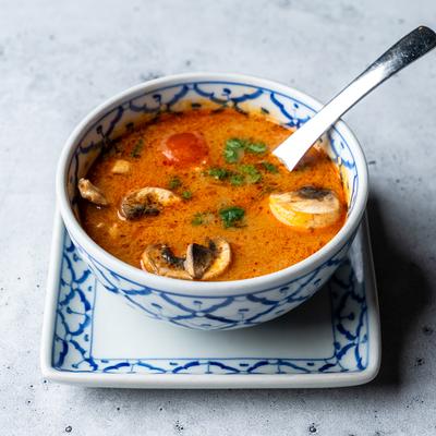 Tom Yum soup with mushrooms, tomatoes, and cilantro.