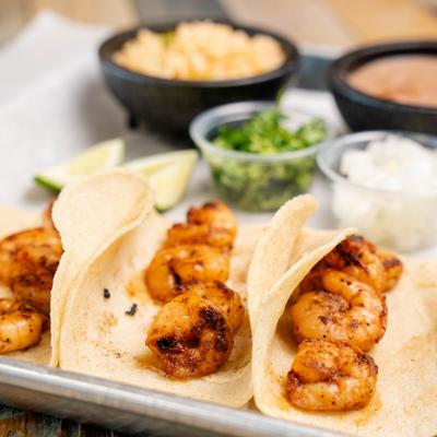 Shrimp tacos served on flour tortillas with sides of rice, lime, cilantro, and beans.