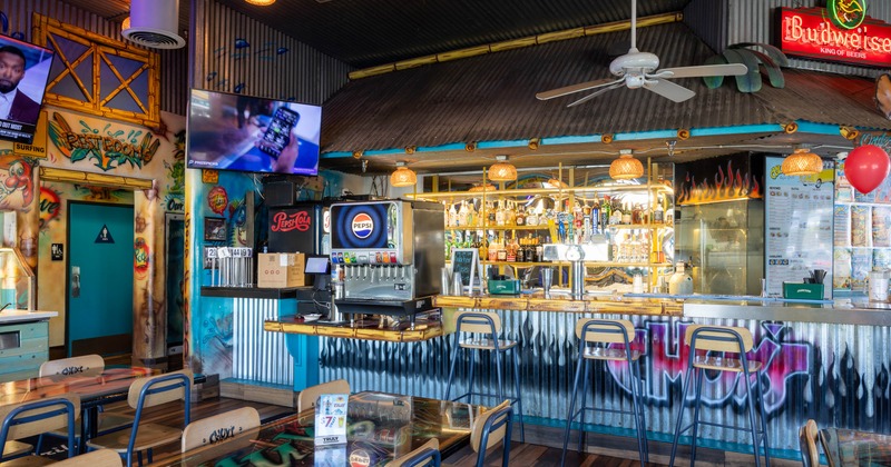 A colorful interior - a graffiti-decorated bar, Pepsi dispenser, vibrant decor, pendant lights, TVs