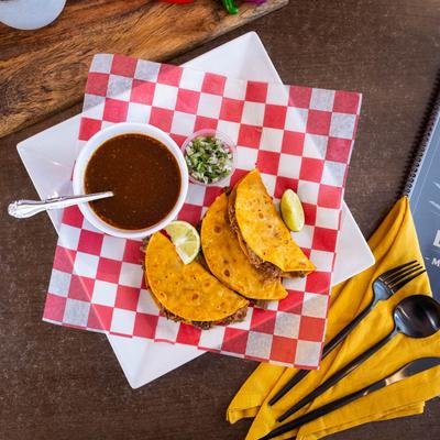 Quesabirria tacos served with consomme, onions, cilantro, and lime.