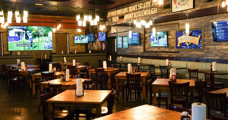 Interior view of a restaurant with wooden tables, pendant lights, and multiple TVs