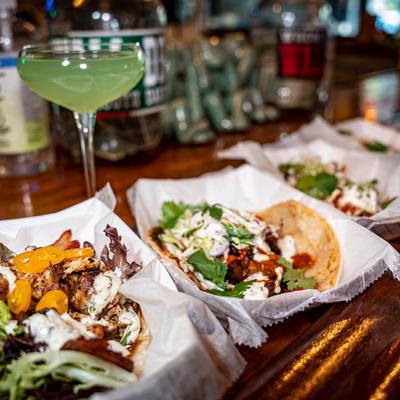 Assorted tacos on a bar counter with a cocktail drink, close up