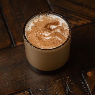 Latte in a glass mug, topped with cinnamon and frothy milk, sits on a rustic wooden table.