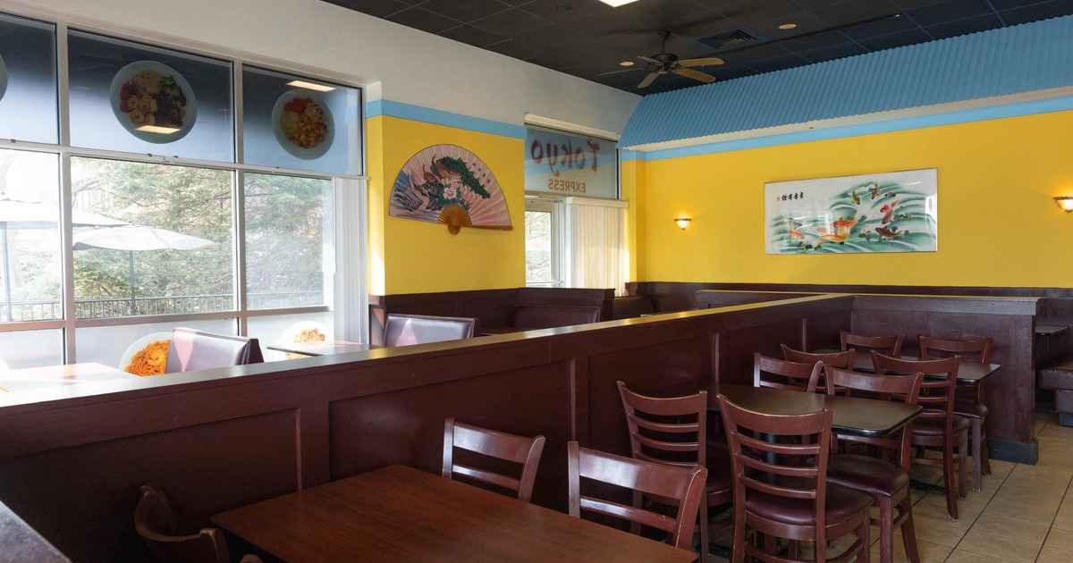 Interior of a restaurant with yellow walls, wooden tables and chairs, and large window