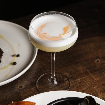 Cocktail in a coupe glass served on the table alongside plates of food.