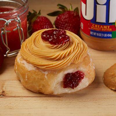 Peanut butter and jelly donut with strawberries, jam, and peanut butter slightly behind.