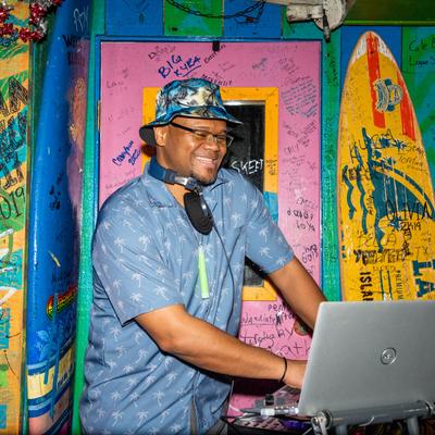 A DJ standing by a laptop in front of a colorful wall.