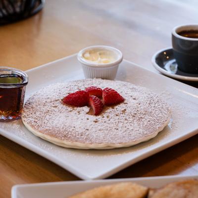 Pancake topped with powdered sugar and sliced strawberries, served with syrup and butter.